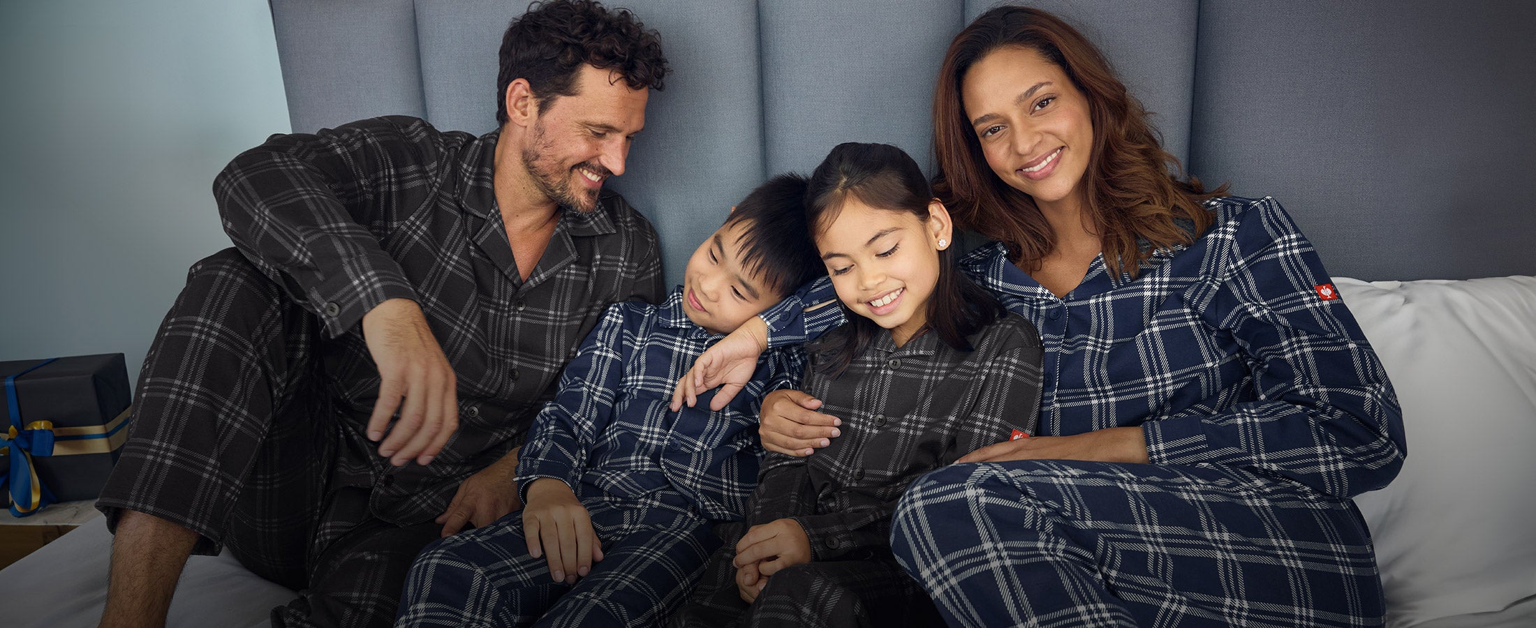 Dame, Mann, Mädchen und Junge tragen e.s. Karo-Pyjamas auf einem Bett