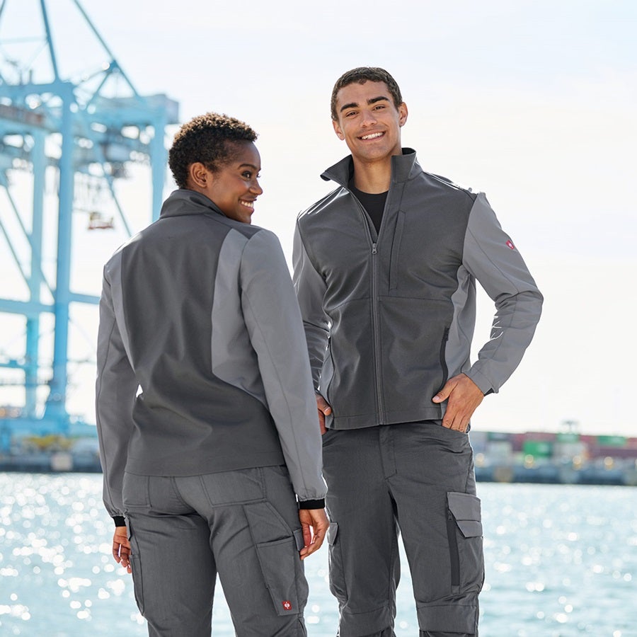 La femme et l’homme portent une veste Softshell e.s.trail pure en gris carbone / gris basalte
