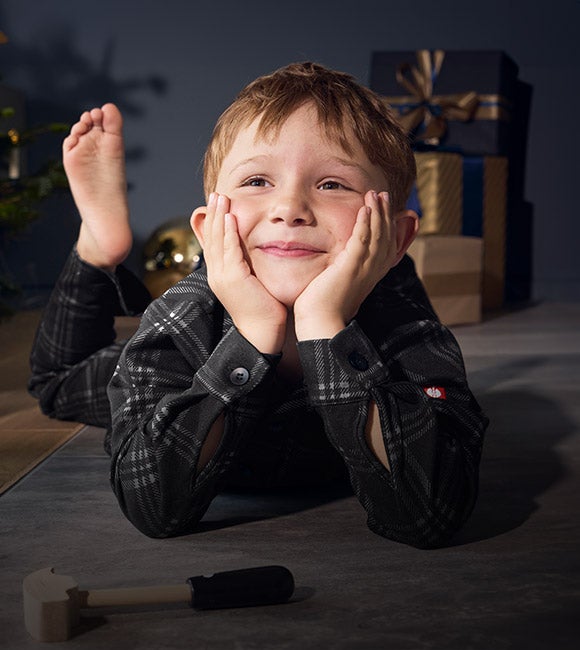 Ein Junge trägt den e.s. Karo-Pyjama in weihnachtlichem Wohnzimmer
